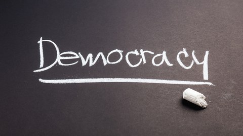 The word “Democracy” is written in chalk on a blackboard. 