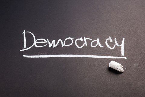 The word “Democracy” is written in chalk on a blackboard. 
