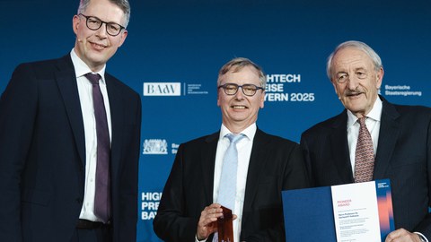 Prof. Fettweis hält lächelnd den Pioneer Award in die Kamera. Neben ihm Markus Blume - Bayerischer Staatsminister für Wissenschaft und Kunst - und Prof. Markus Schwaiger - Präsident der Bayerischen Akademie der Wissenschaften.
