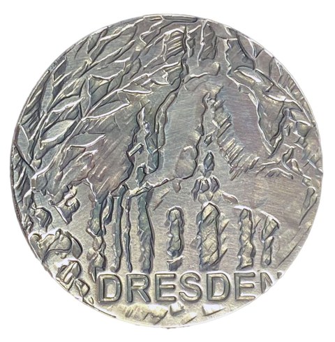 Foto von der Vorderseite der Ehrenmünze der Landeshauptstadt Dresden. Sie zeigt neben dem Stadtwappen auch die Frauenkirche Dresden und einen Lorbeerzweig.