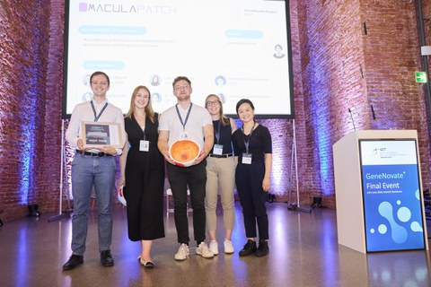 Das Foto zeigt das MaculaPatch-Team, bestehend aus 5 Personen, mit Auszeichnung und Augenmodell vor der GeneNovate®-Bühne in der Allerheiligen Hofkirche in München