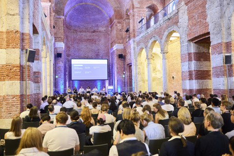 Das Foto zeigt das Innere eines Kirchenschiffs, verwandelt in einen großen Veranstaltungssaal, mit Publikum und einer Paneldiskussion auf der Bühne.