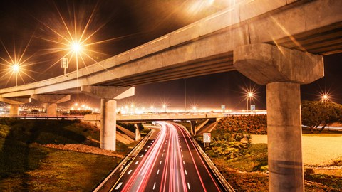 Das Foto zeigt unscharf die Lichter und den schnellen Verkehr auf einer Autobahn in der Nacht.