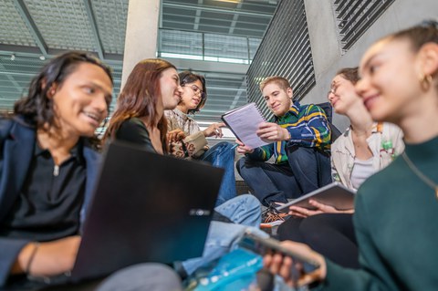 Foto von sechs Studierenden, die auf dem TUD-Campus auf einer Treppe sitzen und zusammen lernen. 