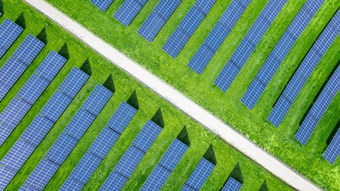Luftbildaufnahme von einer großen Solaranlage mit Reihen moderner Photovoltaik-Solarmodule auf einem Feld.