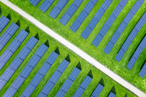 Luftbildaufnahme von einer großen Solaranlage mit Reihen moderner Photovoltaik-Solarmodule auf einem Feld.