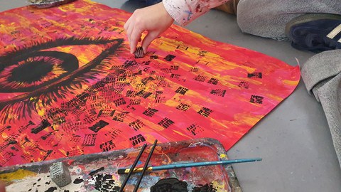 Ein schwarzes Auge auf rotem Hintergrund wird gemalt.