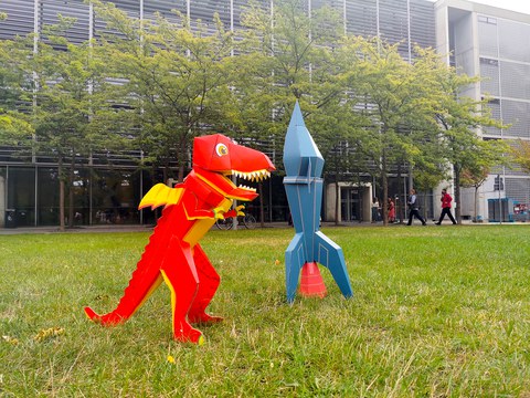Ein Drache und eine Rakete aus Pappe stehen vor dem Hörsaalzentrum.