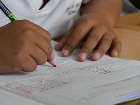 Zwei Kinderhände, es wird mit einem Bleistift in ein Heft geschrieben.