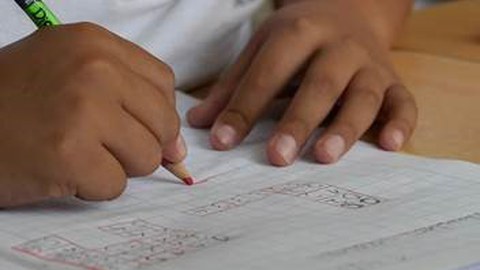 Zwei Kinderhände, es wird mit einem Bleistift in ein Heft geschrieben.