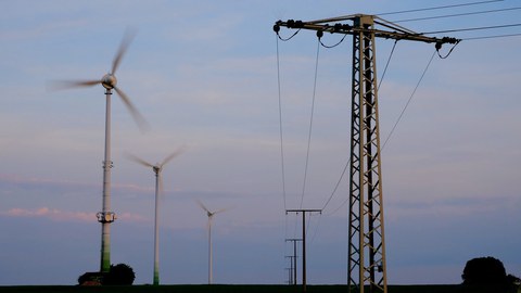 Am linken Bildrand sind Windräder zu sehen, am rechten ein Oberleitungsmast