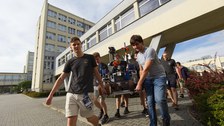 Mehrere Männer tragen den Mars-Rover über einen gepflasterten Weg.