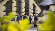 Personengruppe vor einem hellen, schiefergedeckten Gebäude.
