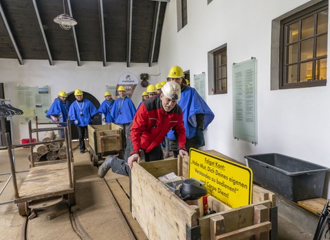 Personen in Schutzkleidung in einem Raum mit Loren.