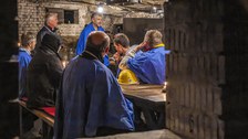 Blick durch eine Öffnung im Mauerwerk auf einen Raum mit Personen in Schutzkleidung.