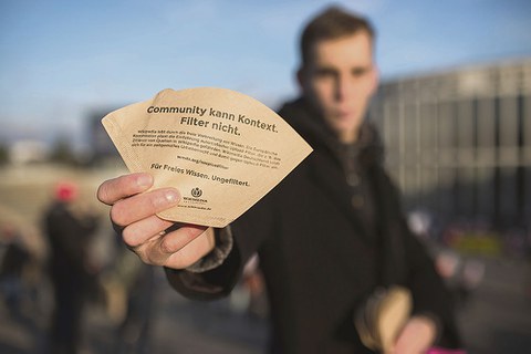 Mann hält Kaffeefilter mit Aufschrift "Community kann Kontext. Filter nicht." in der Hand.