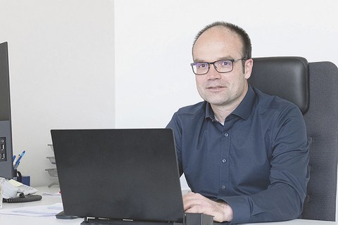 Prof. Lars Bernard sitzt am Schreibtisch. Vor ihm steht ein aufgeklapptes Laptop, auf dem er tippt. Prof. Bernard sieht den Betrachter an.