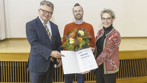 Dr. Jens Bornschein hält einen Blumenstrauß in der Hand. Links neben ihm steht Rektorin Prof. Ursula M. Staudinger, links Burkhard von der Osten. Beide halten die Urkunde in Richtung Betrachter.