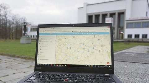 Ein geöffneter Laptop steht auf einem Weg vor dem Hygiene-Museum Dresden. Auf dem Bildschirm ist die Lernlandkarte Sachsen geöffnet.