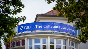 Foto eines blauen TUD-Banners mit dem TUD-Logo und der weißen Aufschrift: "The Collaborative University." an der Zebradiele.