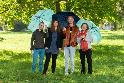 Drei Frauen und ein Mann mit blauen Schirmen
