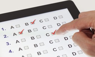 Das Foto zeigt ein Tablet, auf dem der Antwortbogen zu einem Test dargestellt wird. Dabei muss man bei einem der Buchstaben von A bis D ein Häkchen setzen. Man erkennt außerdem die Hand einer Person.