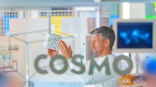 Foto: Person hält einen weißen Würfel mit schwarzen Punkten vor einem Gitterrahmen in der COSMO Wissenschaftsausstellung in der Dresdner Altstadt..