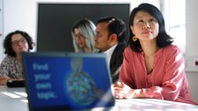 Foto: Beschäftigte bei einer Weiterbildung, sitzend an einem Tisch, im Vordergrund ein Laptop mit der Aufschrift 'Find your own topic'.