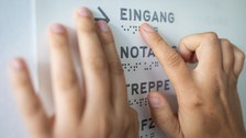 Photo of two hands touching Braille characters on a swell paper.