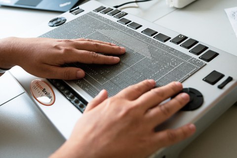 Photo of two hands lying on a Metec Hyperbraille. The pins represent the outlines of a house.