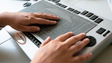 Photo of two hands lying on a Metec Hyperbraille. The pins represent the outlines of a house.