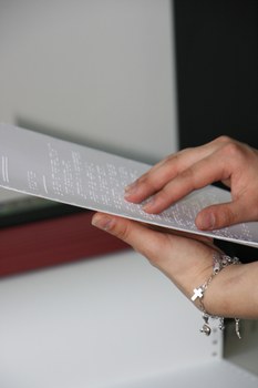 Photo of a Braille printout. One hand is holding the paper, the other is feeling the Braille.