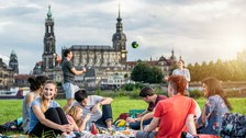 Foto: Gruppe von Studierenden an der Elbe. Sie spielen Volleyball und sitzen plaudernd auf der Wiese.