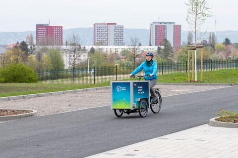 Foto einer Frau, die mit einem Lastenfahrrad des Green Office durch die Stadt fährt.