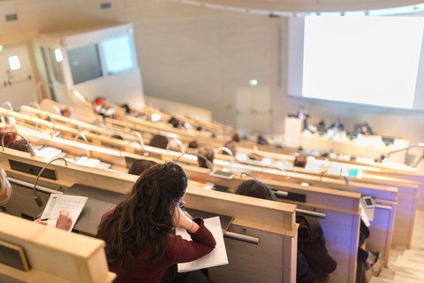 Foto: Studierende sitzen in einem Hörsaal und machen Notizen während einer Vorlesung.