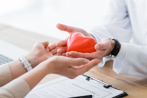 Die Hände eines Arztes halten ein rotes Herz in der Hand. 