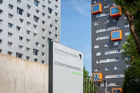 Im Vordergrund ist ein Schild mit der Aufschrift Studentenwohnheime zu sehen, im Hintergrund die Wohnheime Hochschulstraße 46 und 48, zwei graue Hochhäuser