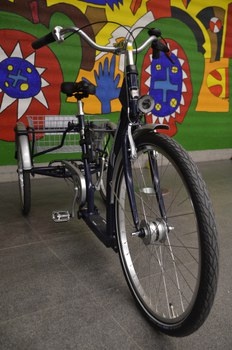 The photo shows one of the service tricycles, which is equipped with lights, a bell and a small luggage basket between the two rear wheels. The tricycle can stand upright without any problems.