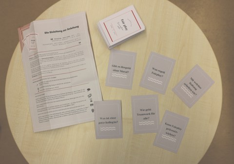 The Fair play card set lies on a table, with the instructions and some cards lying next to it, giving an insight into the questions the game asks.
