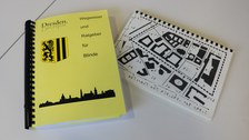 Photograph of the ring binder with explanations of maps of individual city areas in Braille, plus tactile maps in a separate booklet