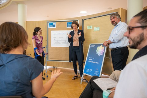 Professorin Böhm und Herr Prof. Ganseuer im Gespräch mit Workshopteilnehmenden. Im Hintergrund stehen Planwände zur Sicherung von Ideen und Ergebnissen.