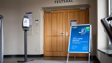 Blaues Infomationsschild vor brauner Tür, welches auf die Veranstaltung hinweist