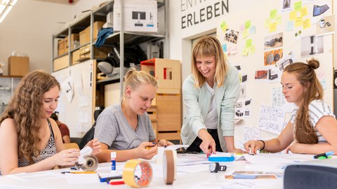 Vier Studentinnen arbeiten gemeinsam an einem Modell. Drei von ihnen sitzen, eine steht.