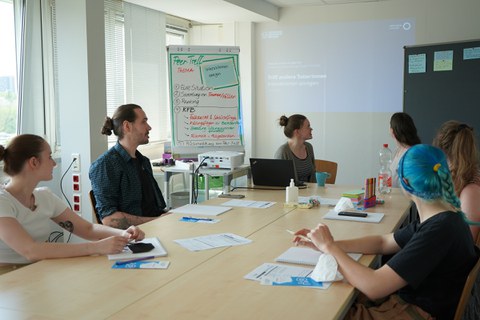 Das Foto zeigt Studierende an einem Tisch die zusammen an eine Tagel schauen und diskutieren.