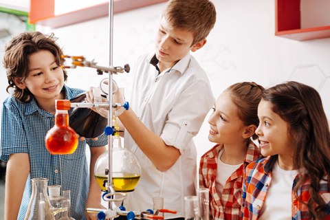 Vier Kinder stehen um ein chemisches Experiment mit Flüssigkeiten