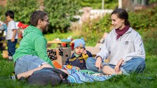 Mann und Frau mit Kleinkind in der Mitte sitzen auf einer Decke auf der Festwiese