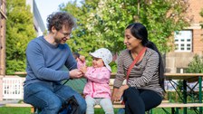 Mann, Kind und Frau sitzen auf einer Bank und Kind isst ein Eis