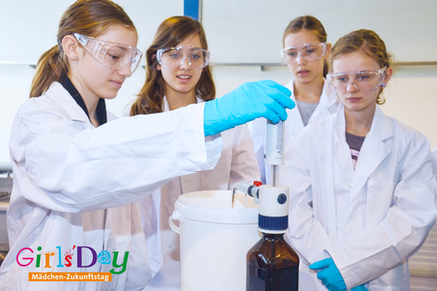 Mehrere Schülerinnen in Laborkitteln und Schutzbrillen arbeiten gemeinsam an einem Experiment im Labor und nutzen dabei ein technisches Gerät; Girls’ Day Logo unten links.