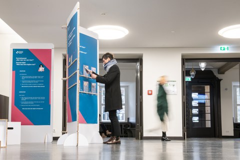 A person examines info panels in a foyer exhibition as others walk by.