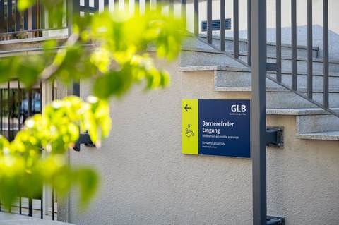 Das Foto zeigt ein Schild mit einem Pfeil und einem Rollstuhlfahrer zum barrierefreien Eingang zum Günther-Landgraf-Bau.